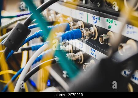 Blaue BNC-SDI-Signalkabel an der Rückseite eines Patchpanels angeschlossen. Eine Unordnung von Kabeln, die hinter dem Rack oder der Verkleidung sichtbar sind. Konzentrieren Sie sich auf einen der Anschlüsse, nicht Stockfoto