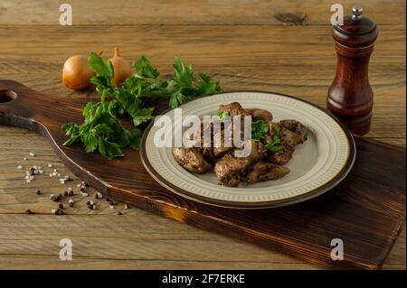 Gekochte Hähnchenleber mit Zwiebeln auf einem Teller, der auf einem Holztisch serviert wird. Rustikaler Stil. Stockfoto