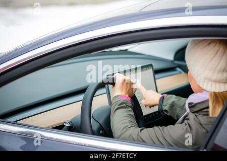 MINSK. WEISSRUSSLAND - JANUAR 2021: Schöne Frau schaut auf einen Laptop eines Elektroautos. Stockfoto