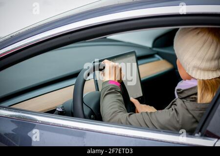 MINSK. WEISSRUSSLAND - JANUAR 2021: Schöne Frau schaut auf einen Laptop eines Elektroautos. Stockfoto