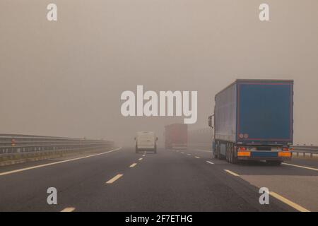 LKW oder Lastwagen und ein Lieferwagen überholen zu einer gefährlichen Zeit mit dichtem Nebel auf einer Autobahn in italien, europa. Stockfoto