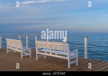 Weiße Holzbänke am Pier mit Blick auf das blaue Meer, Wolken schönen Himmel Stockfoto