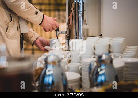 Eine unbekannte weibliche Person gießt während eines Banketts in einer Tasse Kaffee aus. Konzentriere dich auf den Becher. Stockfoto