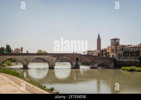 Blick auf die berühmte Ponte Pietra in Verona, die sich über dem Fluss Etsch in Italien erhebt. Langzeitbelichtung bei Tageslicht, aufgenommen an einem sonnigen Tag einer alten Backsteinbrücke Stockfoto