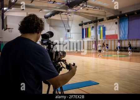 Ein professioneller Videofilmer macht Videoaufnahmen von einem Basketballteam bei einem Training in einem Fitnessstudio. Stockfoto