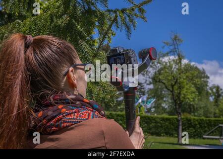 Junge Frau, die an einem sonnigen Tag mit einer professionellen, modernen Spiegelkamera Aufnahmen mit einem Gimbal-Kamerastabilisator im Freien gemacht hat. Stockfoto