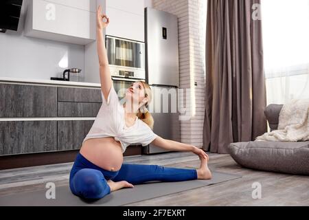 Junge schwangere Dame macht Fitness und Yoga Übungen auf grauen Matte zu Hause. Gesunde Schwangerschaft, Sport und Lifestyle-Konzept. Frau erwartet Baby, Blei Stockfoto