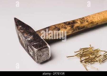 Ein gebrauchter und abgenutzter hammer im europäischen Stil mit Holzgriff und Metallspitze und einigen goldenen Nägeln. Isoliert auf weißer reflektierender Platine. Goldene Nägel sind l Stockfoto