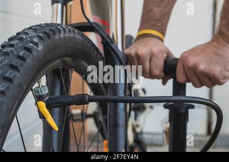 Die Hände eines Mannes sahen, wie er einen Fahrradreifen mit einer eigenständigen Handpumpe pumpte. MTB-Reifen werden an einem bewölkten Tag vor dem Haus aufgepumpt. Stockfoto