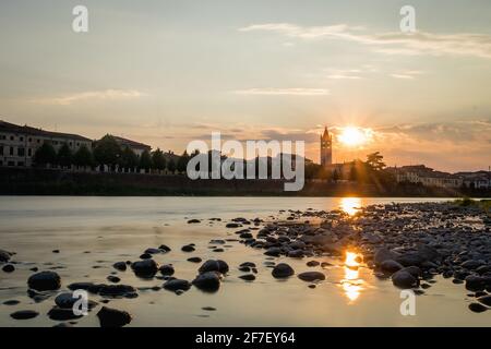 Blick auf die Basilica di San Zeno Maggiore in Verona bei Sonnenuntergang über der Etsch mit Spiegelung auf dem Wasser. Romantisches Bild einer Kirche in Stockfoto