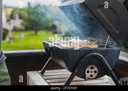 Rauch, der aus einem Smokestack eines kleinen schwarzen Räuchergrills oder Grills kommt, beladen mit Hühnerfleisch und Gemüse. Stockfoto