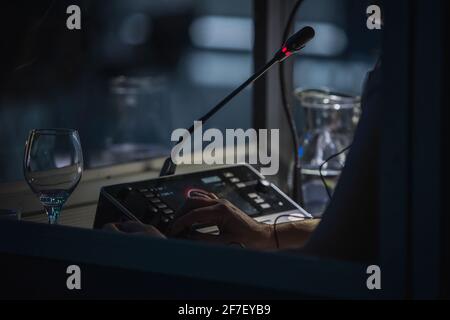 Übersetzer oder Übersetzungsbüro auf einer Konferenz. Die Hand einer Person zum Simultanübersetzen wird in einem Stand gesehen. Ein Glas Wasser neben einem Stb Stockfoto