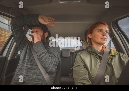 Eine Frau fährt ruhig ein Auto und ein Mann auf dem nächsten Sitz hat Angst wie die Hölle. Völlig verängstigte Beifahrerin wegen des rücksichtslosen fahrlässigen Fahrens durch eine Frau Stockfoto