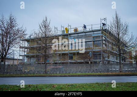 Metallgerüst an einem neuen Gebäude, das im Herbst bei kaltem Wetter gebaut wird. Auf dem Dach des Gebäudes sind Arbeiter zu sehen. Stockfoto