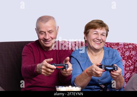Das ältere Paar mittleren Alters begeistert sich leidenschaftlich für Autorennen und sitzt auf einer Couch zu Hause auf dem Sofa vor dem fernsehbildschirm und spielt mit Stockfoto