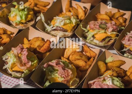 Zubereitung von Gourmet-Burgern oder Hamburgern mit Kartoffeln, Speck, Käse, Brötchen. Detail von halbgemachten Burgern in Pappkartons Stockfoto