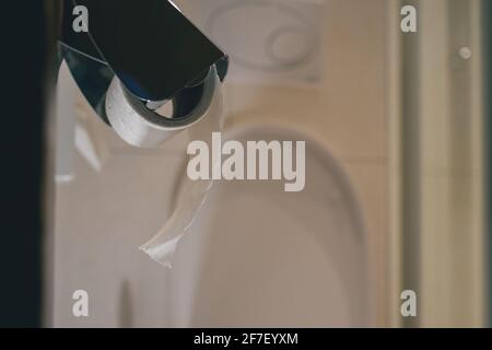 Toilettenpapierrolle auf einem Kleiderbügel im Hotelbadezimmer. Sichtbare Toilette und Spültaste im Hintergrund. Konzept der Verwendung von Toilettenpapier im Hotel. Stockfoto