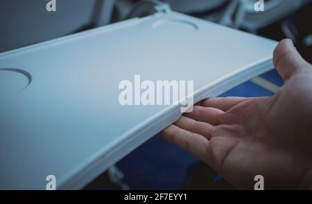 Der Mann schließt oder verstauen die Tischschale auf einer Rückenlehne des Flugzeugsitzes. Sichtbares Tablett in geöffneter Position mit der Hand einer Person, die es schließt. Stockfoto