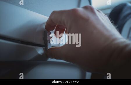 Man öffnet den Knopf zum Lösen der Tischschale an der Rückenlehne eines Flugzeugsitzes. Sichtbares Tablett in verstauter Position mit der Hand einer Person, die den Knopf dreht. Stockfoto