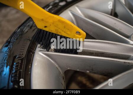 Reinigung von Leichtmetallfelgen oder Leichtmetallfelgen eines Autos mit einer gelben Bürste. Hartnäckigen Bremsstaub mit einem Reinigungslösemittel und einer bru reinigen Stockfoto