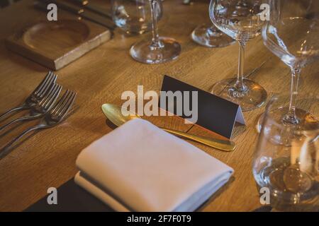 Leerer Namensschild auf einem Holztisch bei einem eleganten Dinner mit mehreren Gläsern, Gabeln und anderem Besteck. Wichtige Person Sitzplatz an einem di Stockfoto