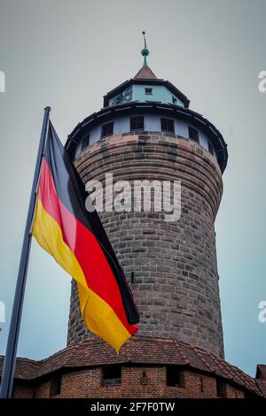 Vertikales Bild des runden Backsteinturms der alten Burg in Nürnberg oder Kaiserburg Nürnberg an einem kalten Herbsttag, vor dem eine deutsche Flagge winkt Stockfoto