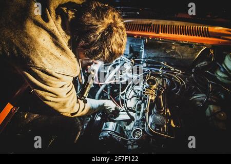 Ein Mann, der nachts einen Motor eines Autos repariert. Oldtimer wird nachts repariert. Schlechtes Timing für eine Autoreparatur. Konzept eines Pech mit einer Ca Stockfoto