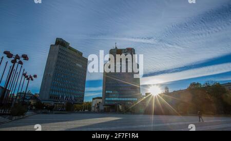 Republic Square oder Trg Republike in Ljubljana, Slowenien bei Sonnenuntergang, mit Sonnenstrahlen, die über die Gebäude und den Betonplatz vor dem Hotel scheinen. Stockfoto