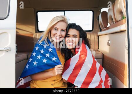 Zwei junge Freundinnen mit amerikanischer Flagge sitzen in einem Wohnmobil. Schöne Frauen mit USA Flagge Stockfoto