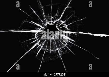 Risse im Fenster von einem Schuss aus einer Waffe. Beschädigtes Fensterglas. Weiße Risse auf schwarzem Hintergrund. Stockfoto