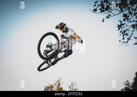 Frontale Aufnahme eines Mountainbiker, der über einen Schmutzsprung in einem Bikepark springt und eine Schwanzpeitsche ausführt. Stockfoto