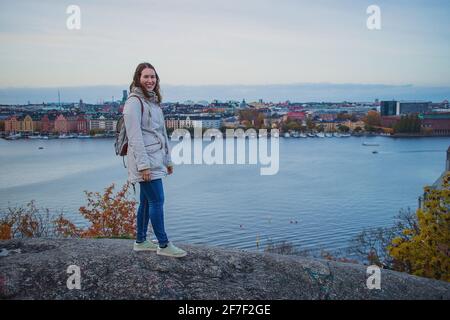 Die junge Frau posiert auf dem Aussichtspunkt Skinnarviksberget, weit über dem Stockholmer Schloss. Das Stadtbild von stockholm ist im Hintergrund zu sehen. Stockfoto