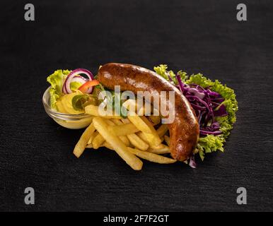 Wurst mit Pommes frites, Senf und Salat Schwarzer Schieferhintergrund Stockfoto