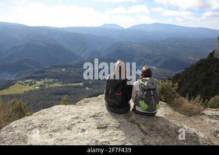 Rückansicht Porträt von zwei Wanderern, die sich ausruhen und Ansichten betrachten Die Spitze einer Klippe in den Bergen Stockfoto