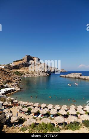 Die Akropolis von Lindian überblickt die St. Paul's Bay in Lindos auf Rhodos, Griechenland. Das antike Denkmal steht unter einem klaren blauen Himmel. Stockfoto