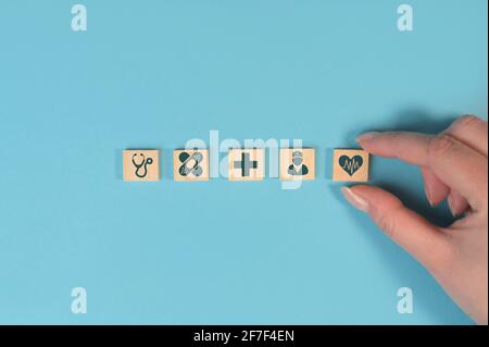 Hand hält Holzblöcke mit medizinischen Symbolen auf blauem Hintergrund mit Platz zum Kopieren. Konzept der Krankenversicherung. Stockfoto