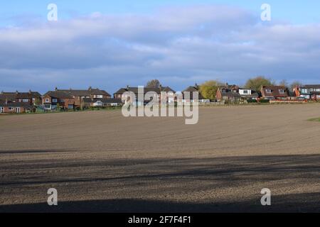 Bauern pflügten Feld am Rande einer Wohnsiedlung mit blauem Himmel mit Kopieplatz Stockfoto