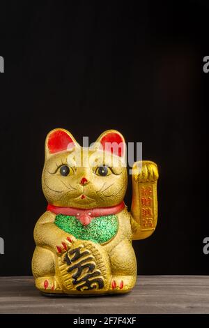 Nahaufnahme von goldenem maneki neko auf Holztisch und schwarzem Hintergrund, senkrecht, mit Kopierraum Stockfoto