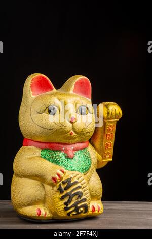 Nahaufnahme von goldenem maneki neko, diagonal, auf Holztisch und schwarzem Hintergrund, senkrecht, mit Kopierraum Stockfoto