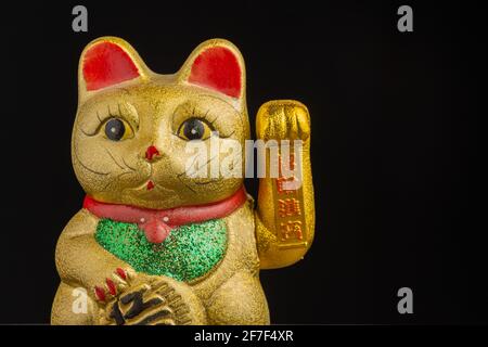 Nahaufnahme Detail von goldenem Maneki Neko mit grünen und roten Tönen, schwarzem Hintergrund, horizontal, mit Kopierraum Stockfoto