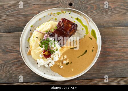 Aus der oberen Ansicht ist das saftige gegrillte Rindersteak mit Kartoffelpüree, Quark, Sauce und Sprossen serviert. Im Restaurant wird ein leckeres Gericht auf einem Holztisch serviert. Küchenkonzept. Stockfoto