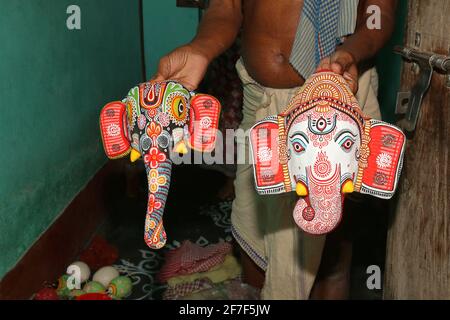 Stammeshandwerker, der in einem Geschäft des Dorfes Raghurajpur in Odisha, Indien, eine handgefertigte Statue des Lord Ganesha-Gesichts aus buntem Papier zeigt Stockfoto