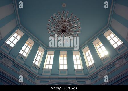 Blick von unten auf den großen Kronleuchter unter der blauen Decke im alten klassischen Gebäude. Das Innere der Wartehalle des Bahnhofs Stockfoto