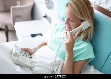 Frau im Bett, die im Hotelzimmer telefoniert Stockfoto