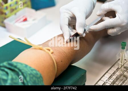 Arzt oder Krankenschwester Hände in medizinischen weißen Handschuhen mit einer Nadelspritze, die Blutprobe aus dem Patientenarm im Krankenhaus entnehmen kann. Stockfoto