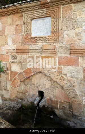 Wasser fließt von einem Brunnen in Lindos auf Rhodos, Griechenland. Die arabische Inschrift auf dem Brunnen ist ein Erbe der osmanischen Herrschaft auf Rhodos. Stockfoto