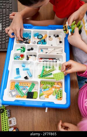 Von oben Blick auf die Hände von Inkognito-Kindern, die Details aus der Box nehmen und an dem Projekt arbeiten. Bunte Stücke aus Baukasten für eine Gruppe von Kindern auf dem Tisch. Konzept für das Engineering. Stockfoto