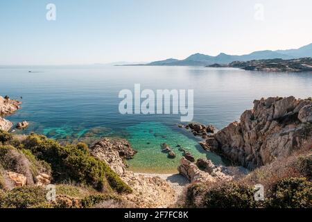 Ein kleiner Kiesstrand und durchscheinendes Mittelmeer auf dem Küste von La Revellata in der Balagne auf Korsika Mit der Zitadelle von Calvi in der Stockfoto