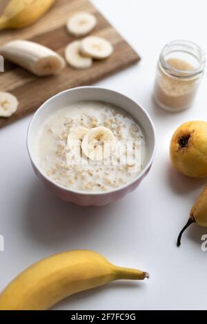 Haferflocken in pflanzlicher Milch mit Scheiben von Banane und Birne auf dem Tisch. Vertikale Zusammensetzung Stockfoto