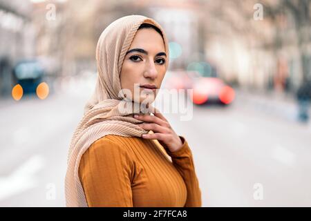 Schöne junge muslimische Frau, die in Hijab auf der Straße steht und die Kamera anschaut. Stockfoto